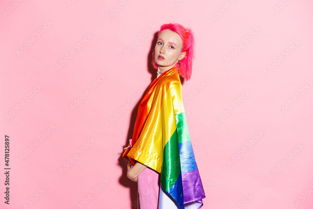 Shirtless woman looking at camera while posing with rainbow flag