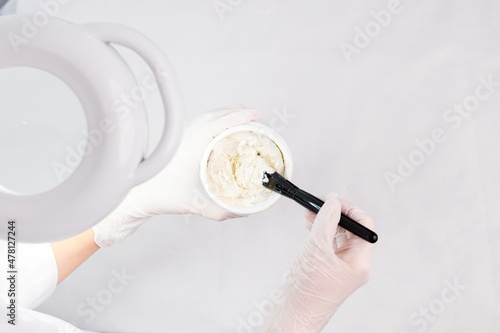 Cosmetologist prepares a rejuvenating mask in a bawl for face procedure wearing white protective gloves.