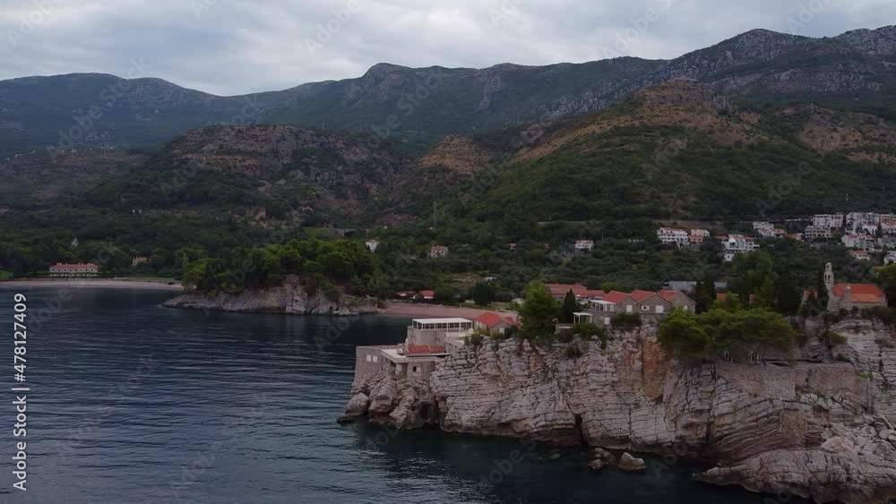 Drone view around the rocky island. Mountain coast in the background. Drone shot of Sveti Stefan (Saint Stephen) island in Montenegro. Drone view around the rocky island. Mountain coast in the background. Drone shot of Sveti Stefan (Saint Stephen) island in Montenegro.