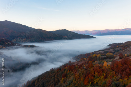 Mountains with colorful trees covered with layer of fog