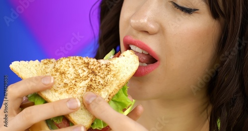 Portrait of a brunette girl eating a sandwich for lunch. A hungry woman is having breakfast.