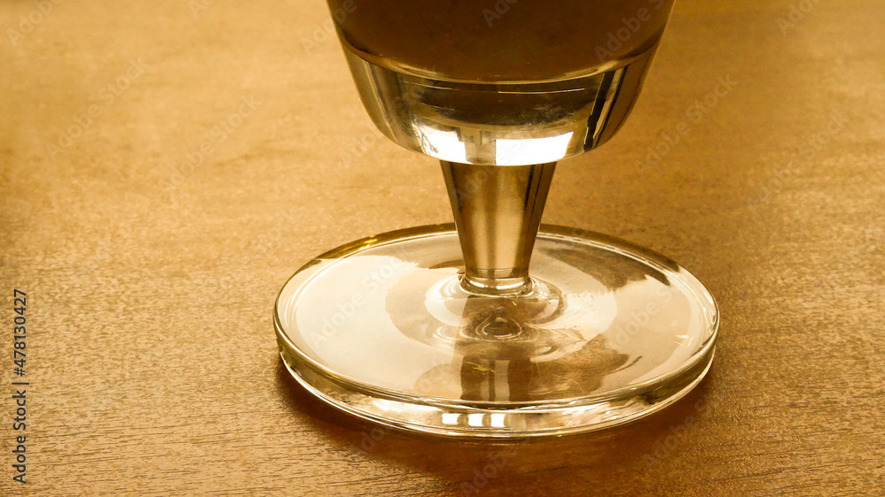 The base of a glass beer glass with a drink on a wooden table top. Golden picture.