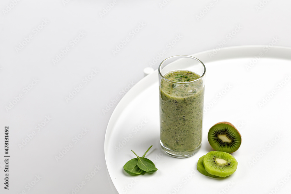 Fototapeta premium Green smoothie in a glass with slices of kiwi and spinach on white round table