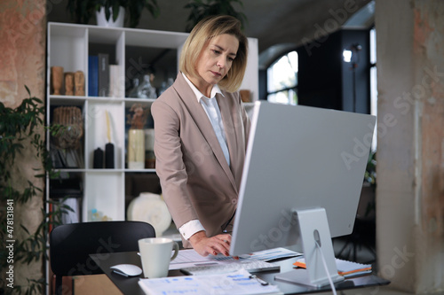 Attractive middle aged woman working at office, using contemporary desktop computer.