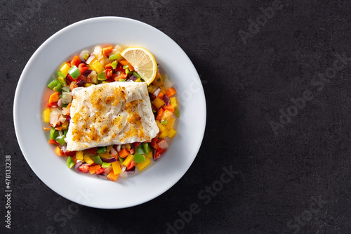 Grilled cod with vegetables in plate on black background. Top view. Copy space