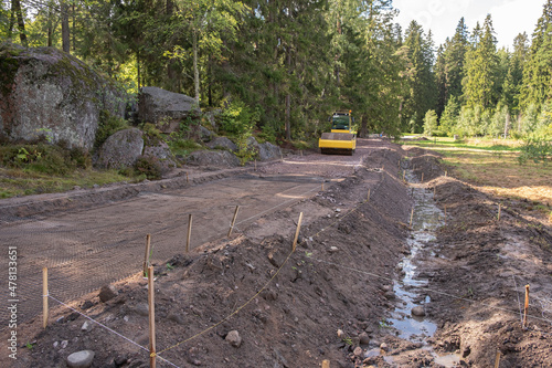 The excavator digs a trench for laying a storm drain and a grid for strengthening the slopes of the mountain at a construction site in a forested area. Construction of a road, drainage ditch and drain photo