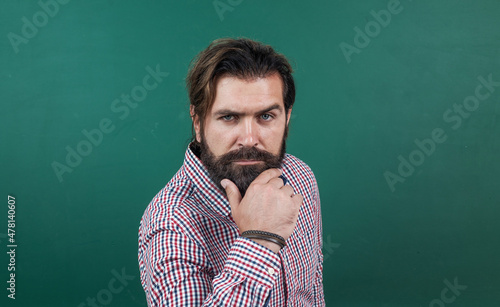 Portrait of a serious mature man standing against green chalkboard, school