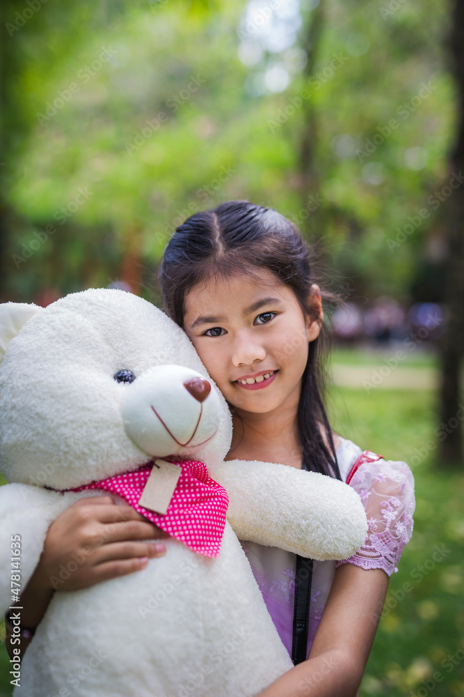 Cute little girl holding white teddy bear is looking at the camera with green nature blurred background Cute little girl holding white teddy bear is looking at the camera with green nature blurred background