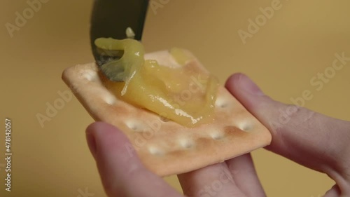 spread honey on a cookie on a yellow background with a knife.