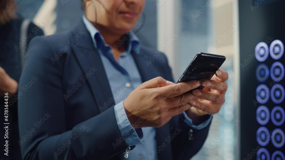 Close up of Black Adult Female Riding Crowded Glass Elevator to Office in Business Center. Successful African American Manager Using Smartphone, Write Message, Check Social Media and Emails in a Lift. Close up of Black Adult Female Riding Crowded Glass Elevator to Office in Business Center. Successful African American Manager Using Smartphone, Write Message, Check Social Media and Emails in a Lift.
