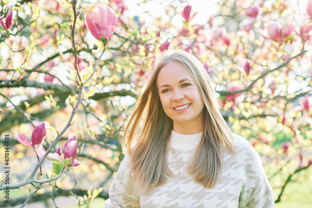 Outdoor portrait of beautiful happy model with blond hair posing next to magnolia flowers Outdoor portrait of beautiful happy model with blond hair posing next to magnolia flowers