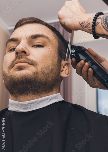 A confident adult man with stubble on his face in hair salon. Cutting man s hair. Hairdressing at home.