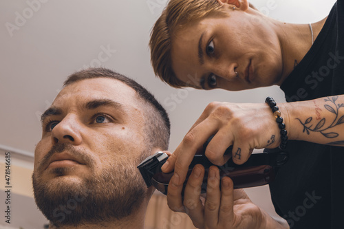 Woman barber uses a hair clipper and styling man's stubble.