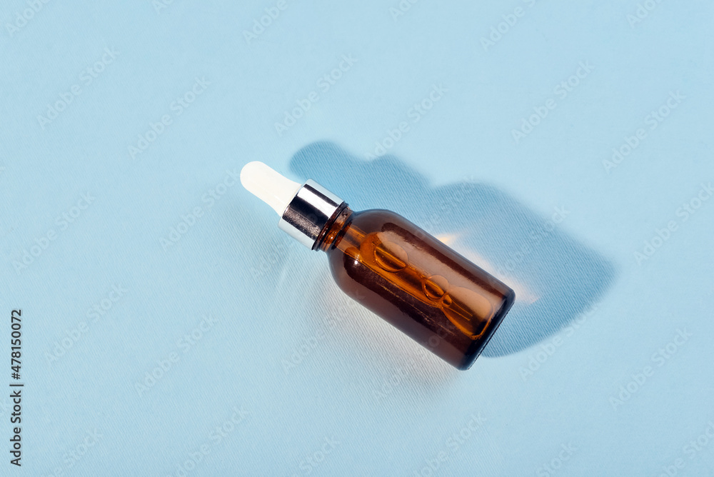 A glass bottle with a pipette with oil, serum brown on a blue background. Flat Lay