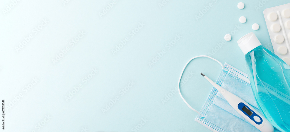 Blue medicine mask , pills, a safe electronic thermometer and a hand antiseptic gel on a blue background. Treatment of colds and flu. Top view, copy space. Medicine banner. Flat lay.