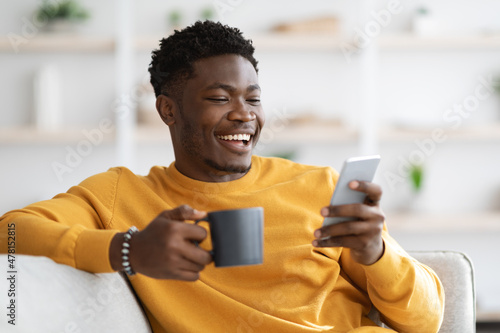 Happy african american guy reclining on couch, using smartphone