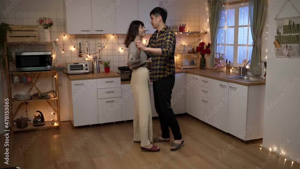 full length of loving asian couple dancing with a spin in the kitchen at a cozy home interior with romantic decoration on valentine’s day night. full length of loving asian couple dancing with a spin in the kitchen at a cozy home interior with romantic decoration on valentine’s day night.