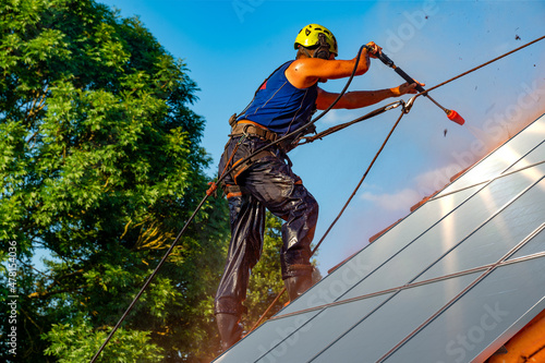Worker washing photovoltaic panels on roof with pressurized water photo