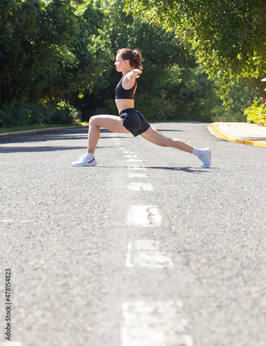 Attractive athletic woman stretching outdoors. Woman stands on the road above road line and doing yoga.