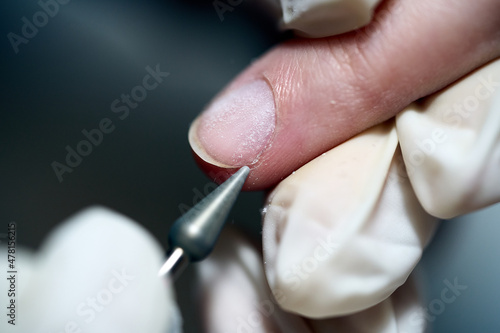 Woman in nail salon receiving manicure in beauty salon by beautician who use electric nail file drill with burst flying dust and debris around. Concept of nail care. 