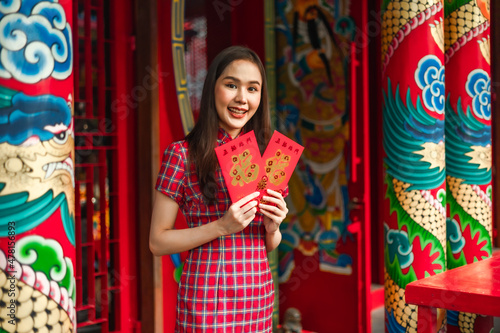 Beautiful Asian woman wearing a traditional red cheongsam on Chinese New Year.Hand holding red envelope or Ang pao with Chinese character means happiness or good fortune. © anon