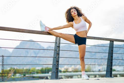 fit and sporty young latin hispanic woman doing stretching in city park