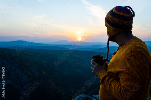man in wooled hat and sweater looking at sun dawn and drinking coffee in nature