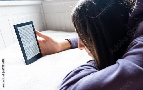 Young Adolescent GIrl is focused reading an electronic romance with her Ebook Reader while she is on the bed. The text on the ebook reader is a 