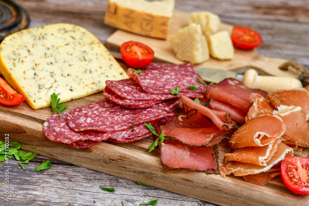 Italian dried thinly sliced artisan pork Salami Milano , mediterranean Parmesan cheese, tomatoes and fresh basil on wooden background .Rustic home made Italian snack. Italian dried thinly sliced artisan pork Salami Milano , mediterranean Parmesan cheese, tomatoes and fresh basil on wooden background .Rustic home made Italian snack.