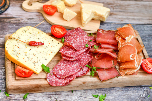 Italian dried thinly sliced artisan pork Salami Milano , mediterranean Parmesan cheese, tomatoes and fresh basil on wooden background .Rustic home made Italian snack.