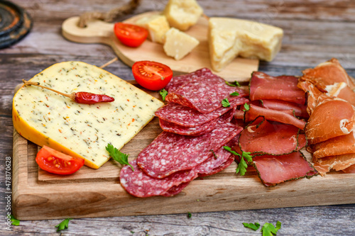 Italian dried thinly sliced artisan pork Salami Milano , mediterranean Parmesan cheese, tomatoes and fresh basil on wooden background .Rustic home made Italian snack.