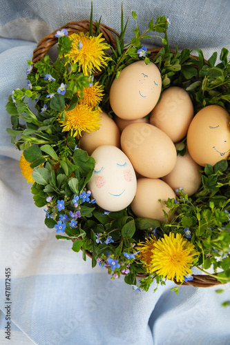 Beautiful spring bouquet in a wooden basket with Easter painted eggs, eggs with cute faces. Easter postcard.