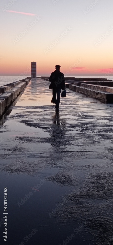 Man walking along the wave breaker at sunset in the Rio Douro mouth
