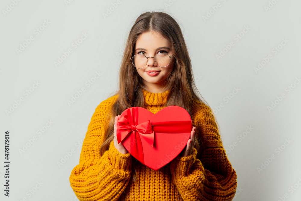 Beautiful girl in glasses and yellow sweater with heart shape gift box on white background Beautiful girl in glasses and yellow sweater with heart shape gift box on white background