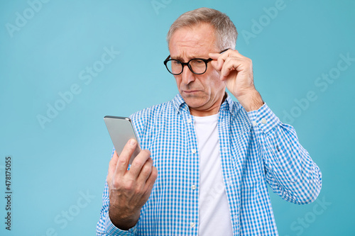 Mature man squinting using mobile phone, looking at screen photo
