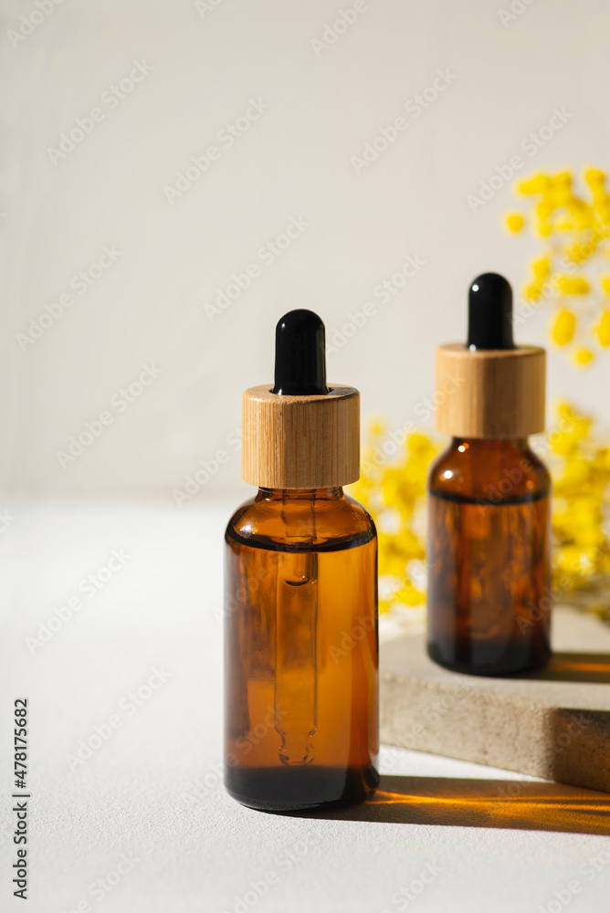 Amber glass bottles with dropper pipette with serum or essential oil on concrete plate for product presentation. Skincare cosmetic with yellow dry plants. Beauty concept for face body care