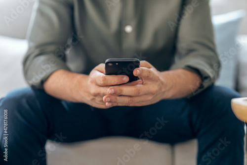 Hands of business man using smartphone texting while relaxing on sofa at home.