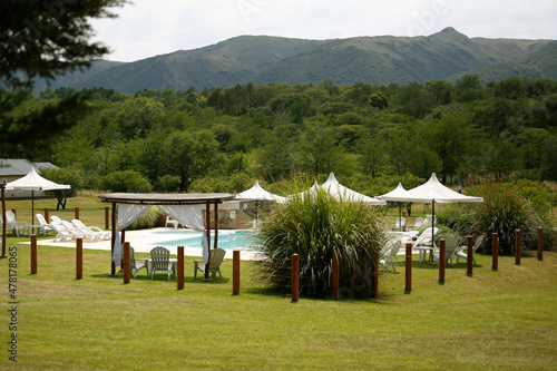  Swimming pool. Recreation, relaxation, vacations, tourism, peace. Nature and mountains. Landscape of Córdoba, Argentine. Umbrellas and lounge chairs. Summer.