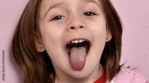 A cute little girl at a maxillofacial surgeon's appointment shows her throat. A wide open mouth sticks out a long tongue, a soft palate and saliva are visible. Focus on the soft palate.