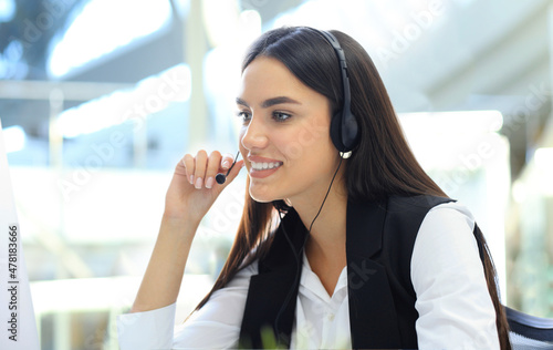 Beautiful young female call center operator with headset in office.