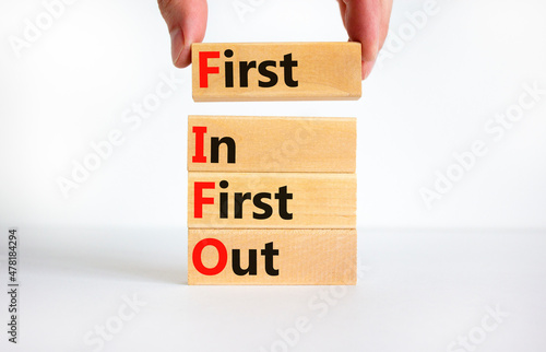 FIFO first in first out symbol. Concept words FIFO first in first out on wooden blocks. Beautiful white table, white background. Businessman hand. Business FIFO first in and out concept. Copy space. photo