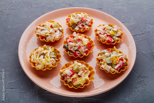 Salad with crab in tartlets on a beige plate on a black background.