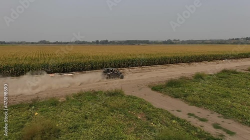 Side by side ATV drives along dirt farm roads next to corn field fast aerial photo