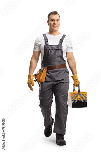Full length portrait of a repairman in a uniform carrying a tool box and walking towards camera
