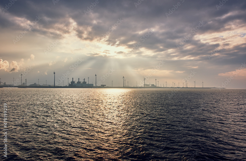 Wind turbine - the sky and the sea, the sun breaks through the clouds, cargo ship at sea