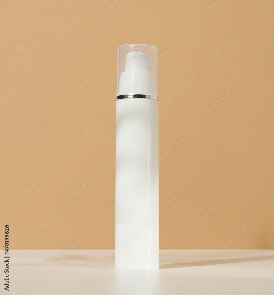 white plastic cosmetic bottle with dispenser and transparent cap on brown background. Packaging for cream, fluid and gel white plastic cosmetic bottle with dispenser and transparent cap on brown background. Packaging for cream, fluid and gel
