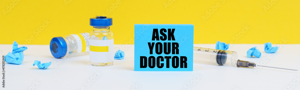 On the table is a syringe, injections and a blue sign with the inscription - ASK YOUR DOCTOR On the table is a syringe, injections and a blue sign with the inscription - ASK YOUR DOCTOR