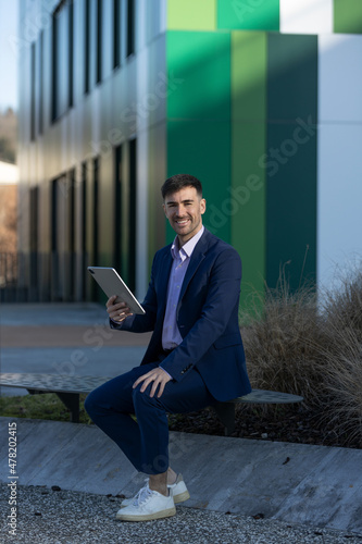 Quadro su tela Business man seated smiling with a tablet in a modern area buildings- Morden sui