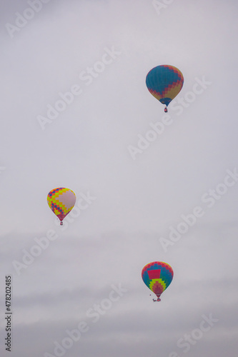 Three colorful hot air balloons flying against grey sky at Winter aerostat festival. Freedom, sport, aircraft concept