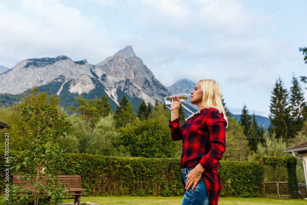 Alps. A woman drinking water from a bottle and admiring the mountain scenery.